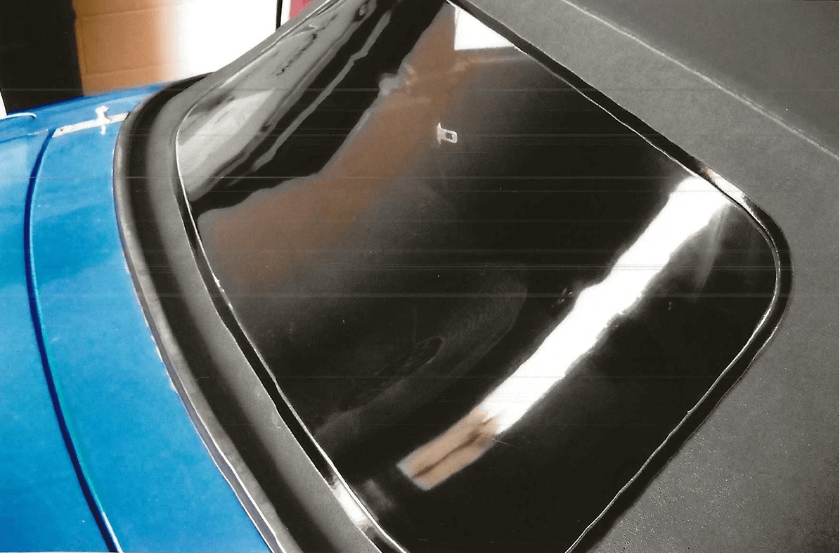 A car's rear windshield with a reflection of a curved light.