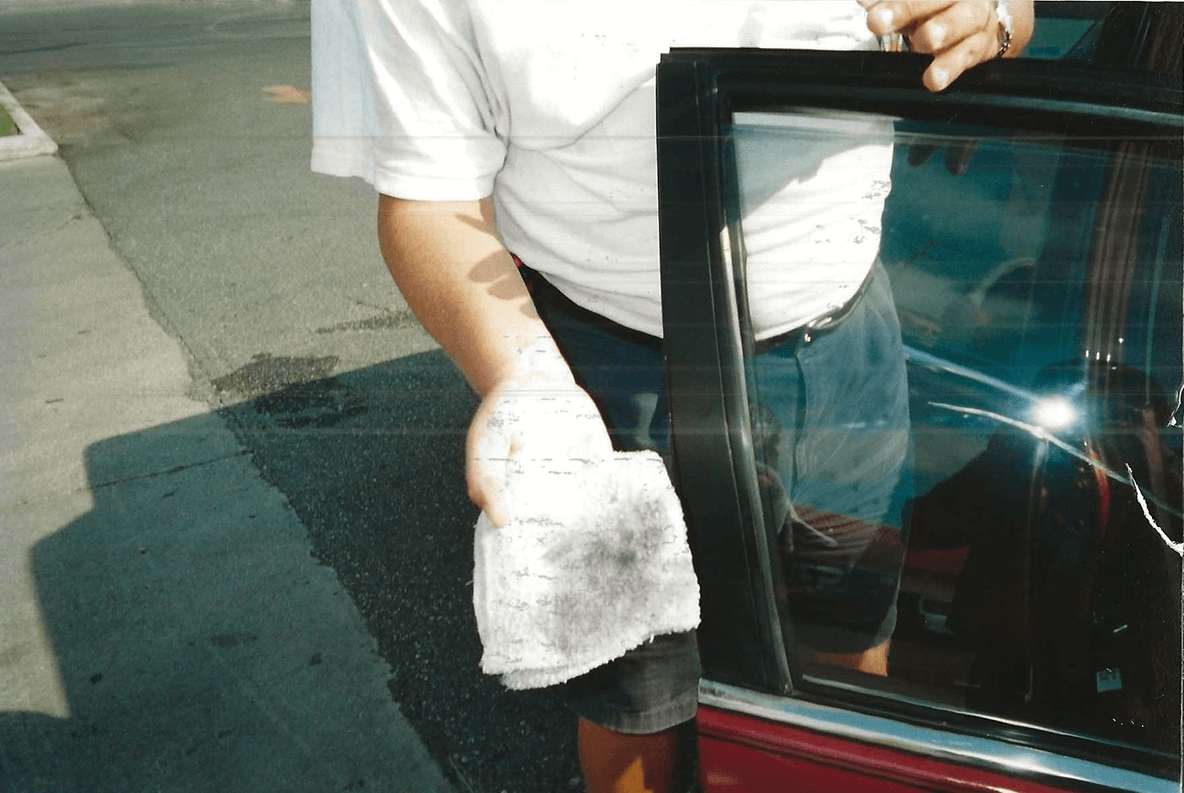 Person cleaning a car door window with a cloth.