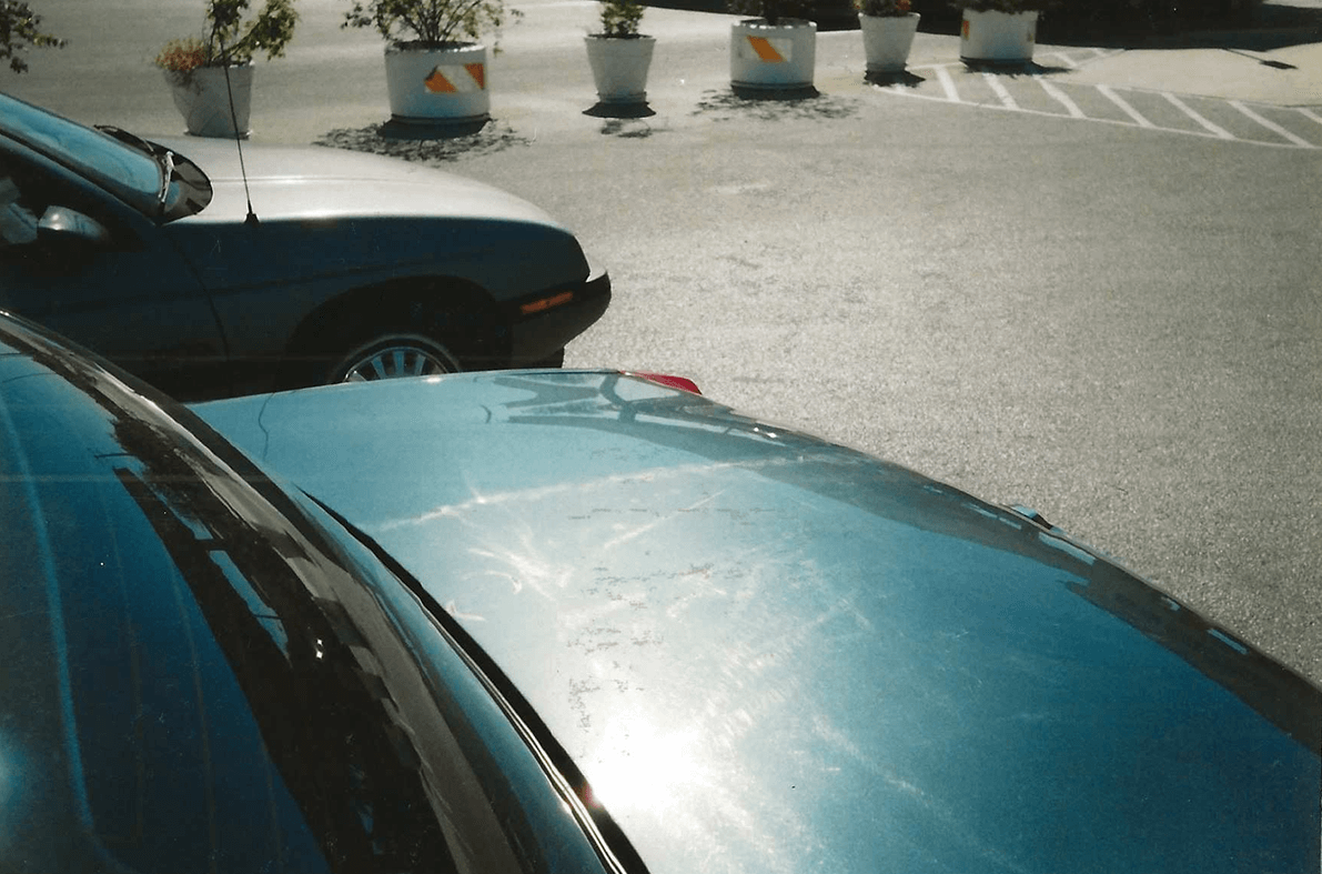 Two cars parked closely on a street with sunlight reflecting off the roof.
