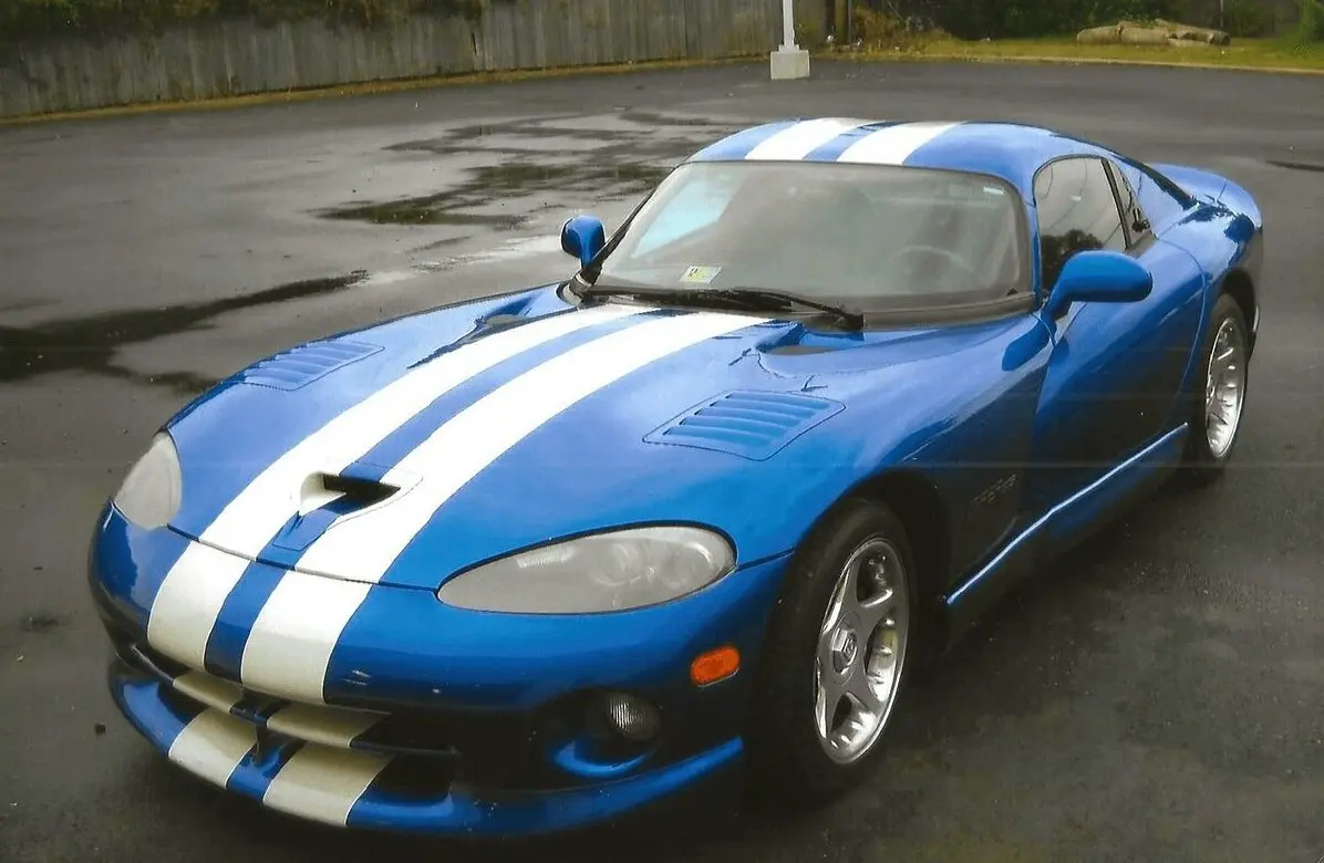 Blue sports car with white racing stripes parked on wet pavement.