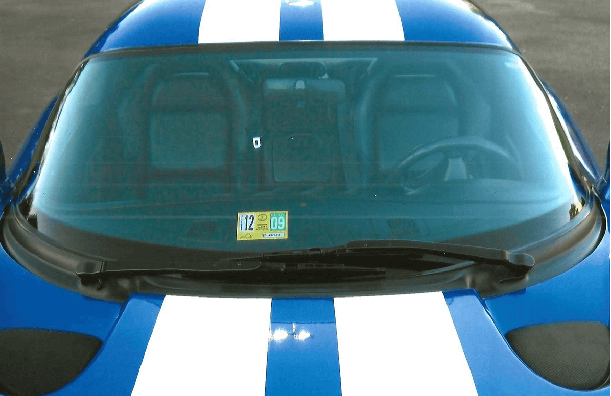 Blue car with white racing stripes and a yellow parking permit on the windshield.